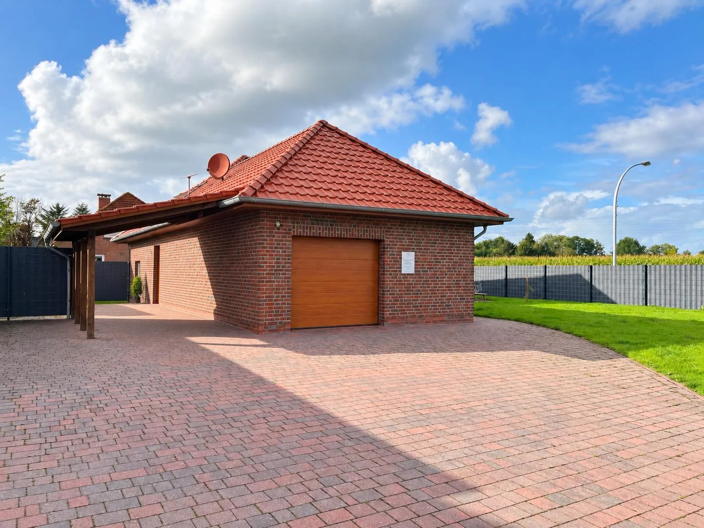 Gepflasterte Einfahrt mit Stellplätzen und Carport neben dem Praxisgebäude